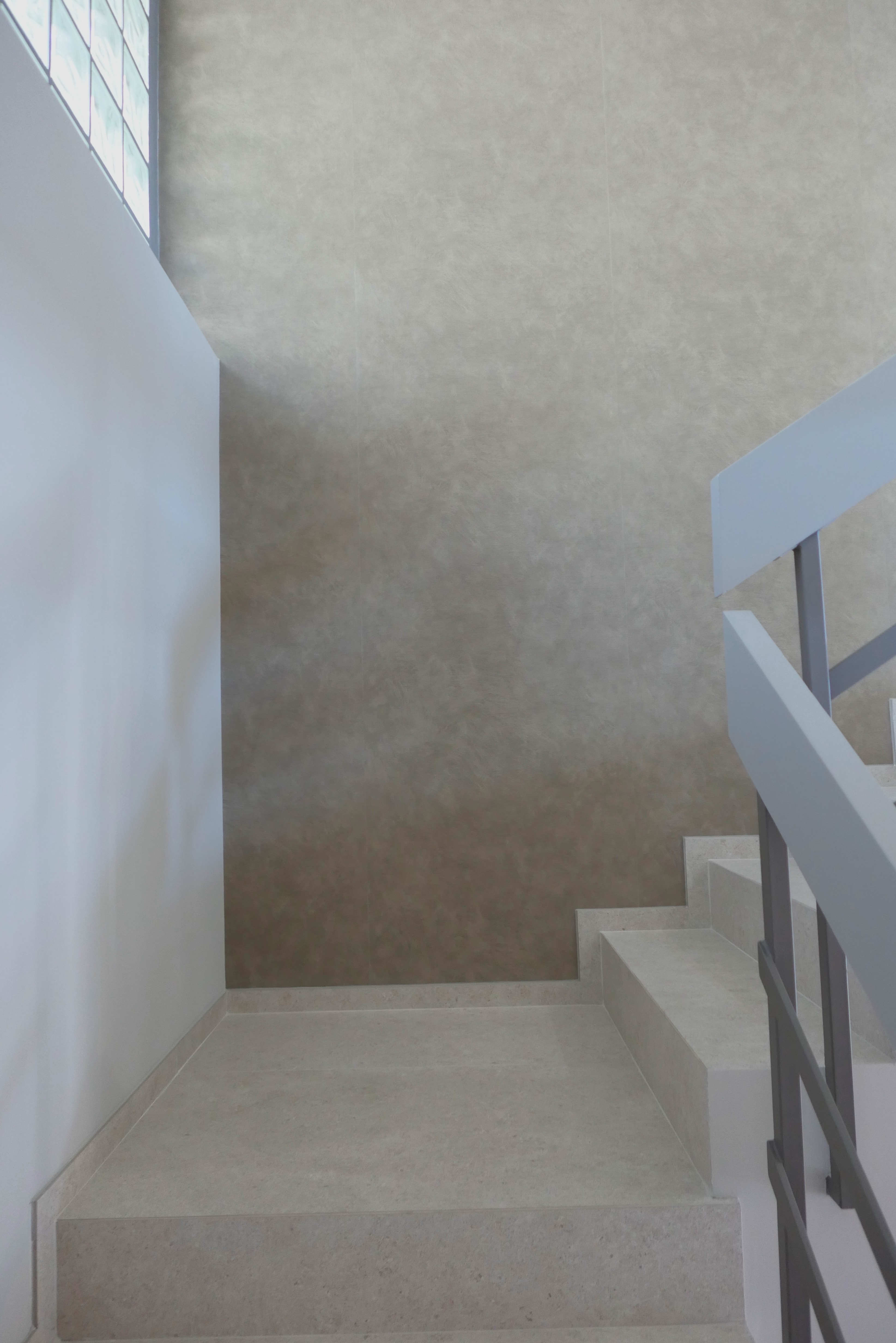 Cage d'escalier : grand mur habillé d'un revêtement décoratif nuagé beige posé en lés, murs voisins en blanc, marches et palier en revêtement clair